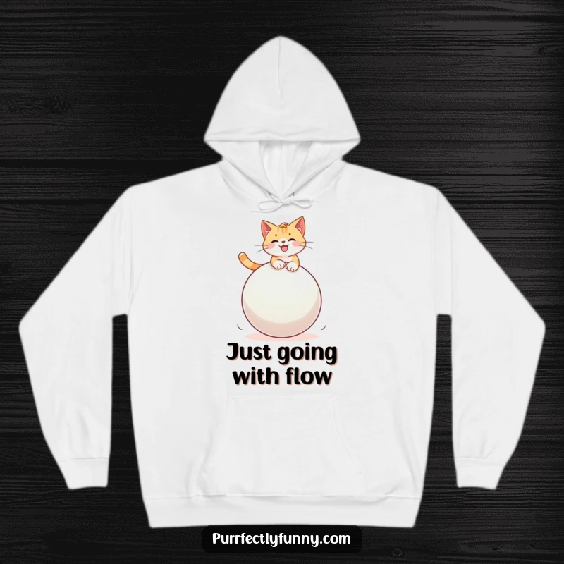 Funny cat balancing precariously on a giant, colorful bouncy ball, bringing immense joy and humor to a cozy hoodie.
